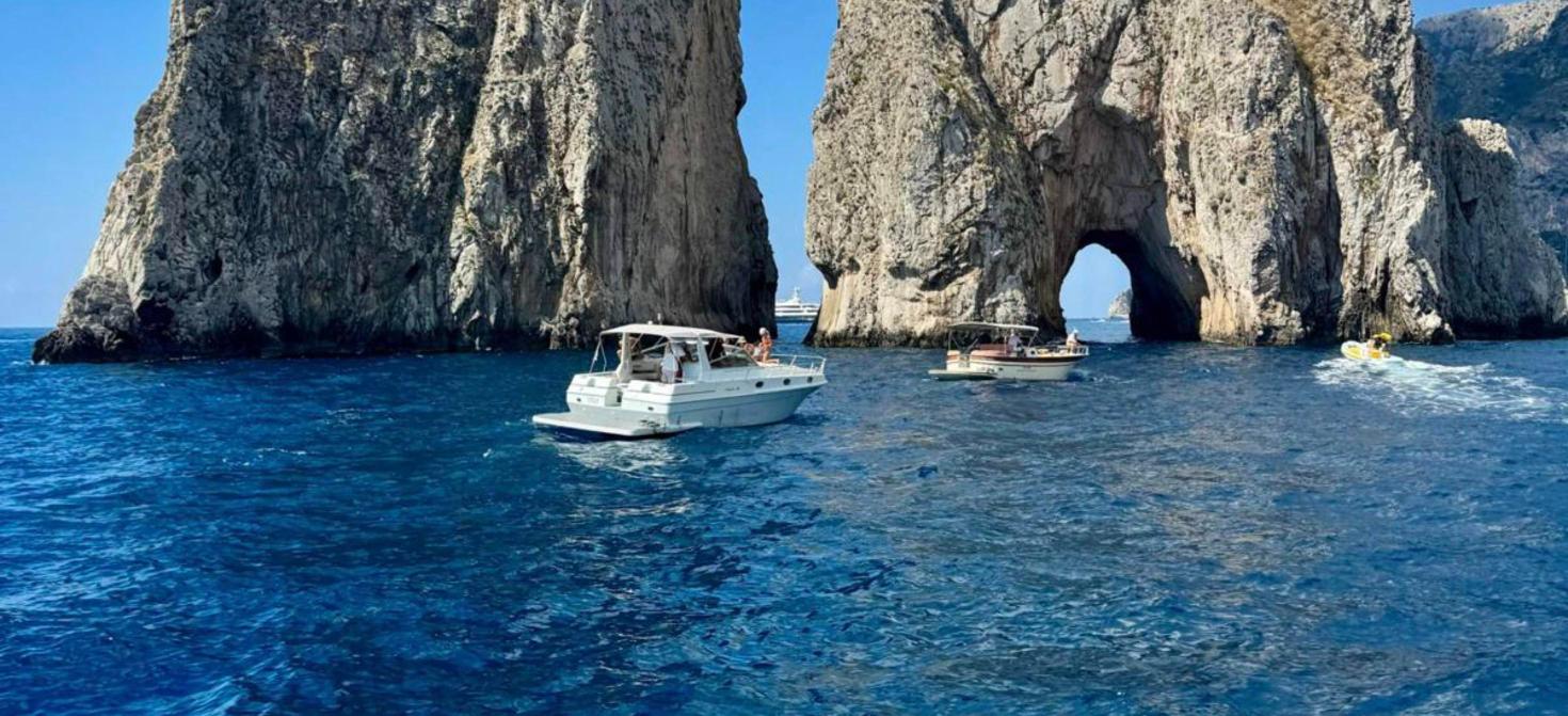 Private boat sailing through the arch of the Faraglioni off Capri