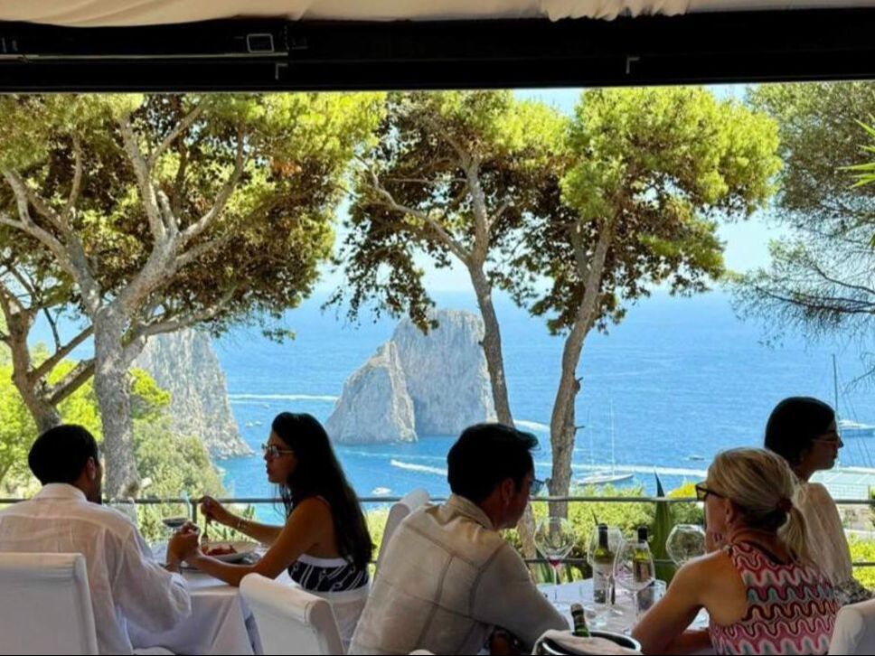 Guests enjoying lunch on a Capri restaurant terrace with a view of the Faraglioni