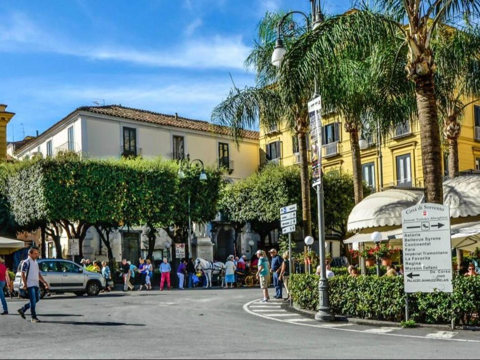 Central square in Sorrento with palm trees, cafes and direction signs