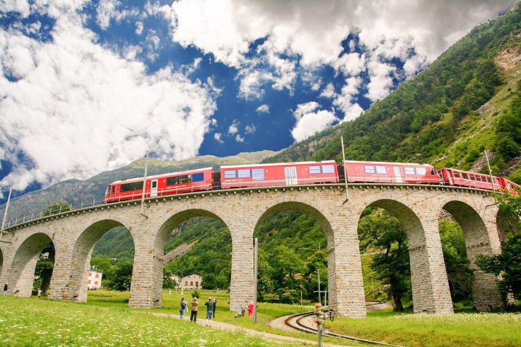 The red Bernina Express train crossing a stone viaduct in the Swiss Alps